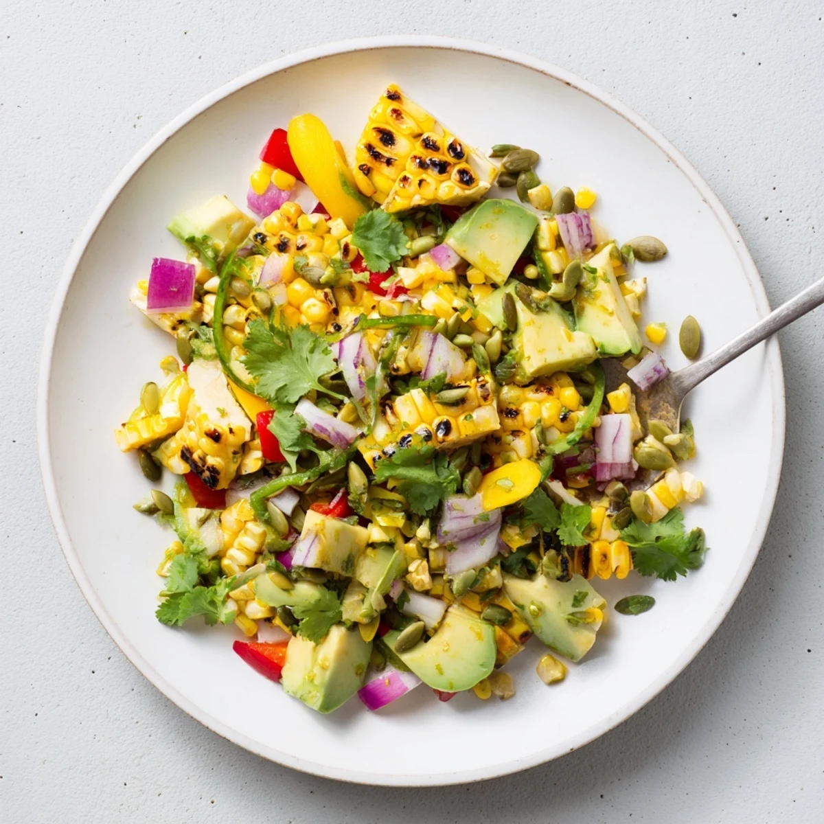 Glowing bowl of tropical charred corn and avocado salad topped with cilantro, pumpkin seeds, and juicy tropical fruits in light dressing.