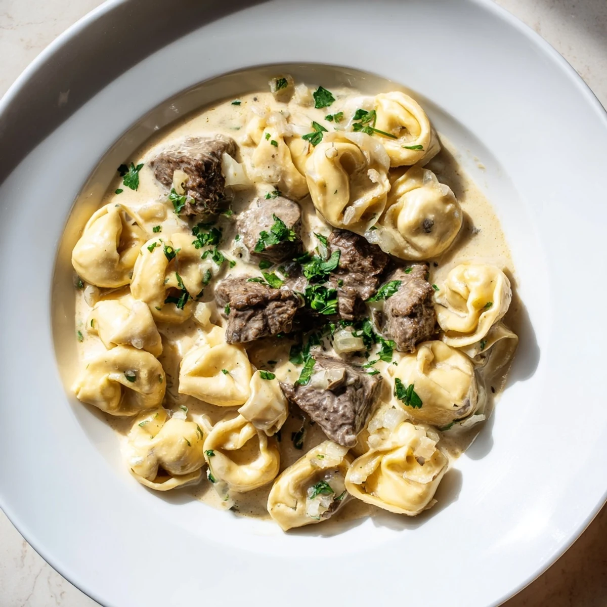 Golden seared steak bites served over cheesy tortellini in rich garlic cream sauce