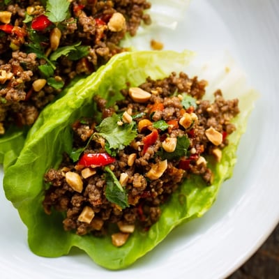 Tender ground beef Lettuce Wraps with Chopped Peanuts served warm with lime wedges on the side, perfect for a light, low-carb appetizer.