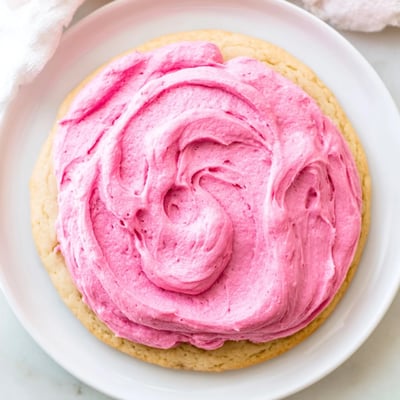 A close-up shows a platter of Crumbl Pink Sugar Cookies with a creamy pink glaze, perfect for a sweet bakery-style treat.