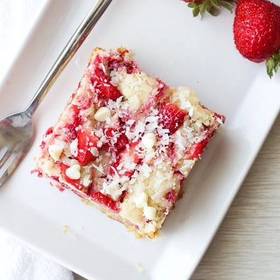 A slice of gooey Strawberry Earthquake Cake reveals white chocolate chips, coconut flakes, and cream cheese ribbons.