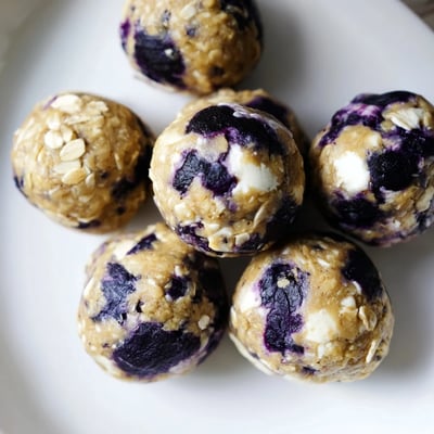 A close-up of Blueberry Cheesecake Protein Bites highlights soft oats, tangy cream cheese, and bursts of sweet dried blueberries.